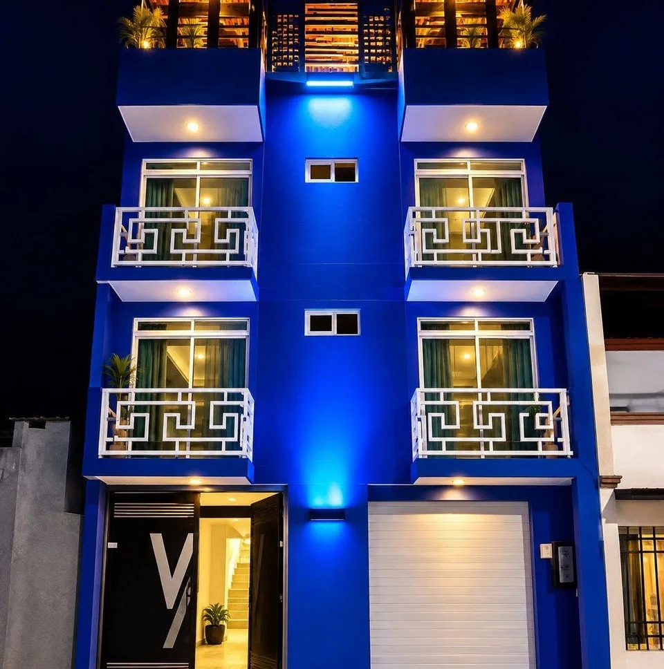 Fachada azul real del edificio LUMA, iluminada de noche y con balcones blancos